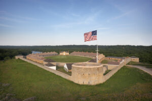 An aerial view of an 1800s-era fort with American flag waving overhead.