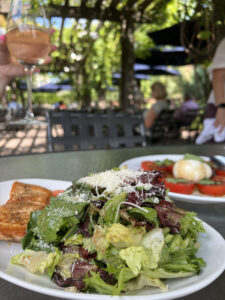 Close-up of a salad, with a person holding a glass of wine in the background, at Ciao Bella