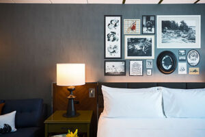 A hotel room bed with lit lamp and gallery wall of art