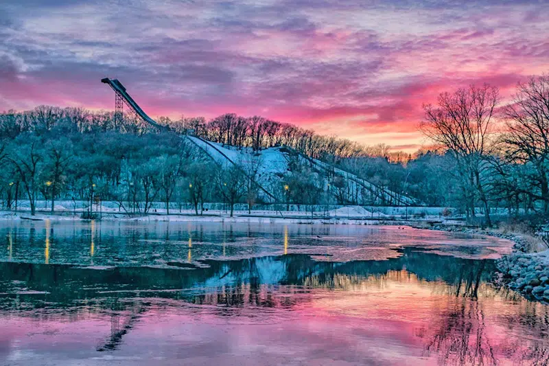 A frozen Bush Lake with the ski jump and a pink sunrise in the background.