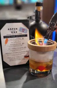 A smoking cocktail next to a menu that reads "Aspen and Oak Lounge and Restaurant"