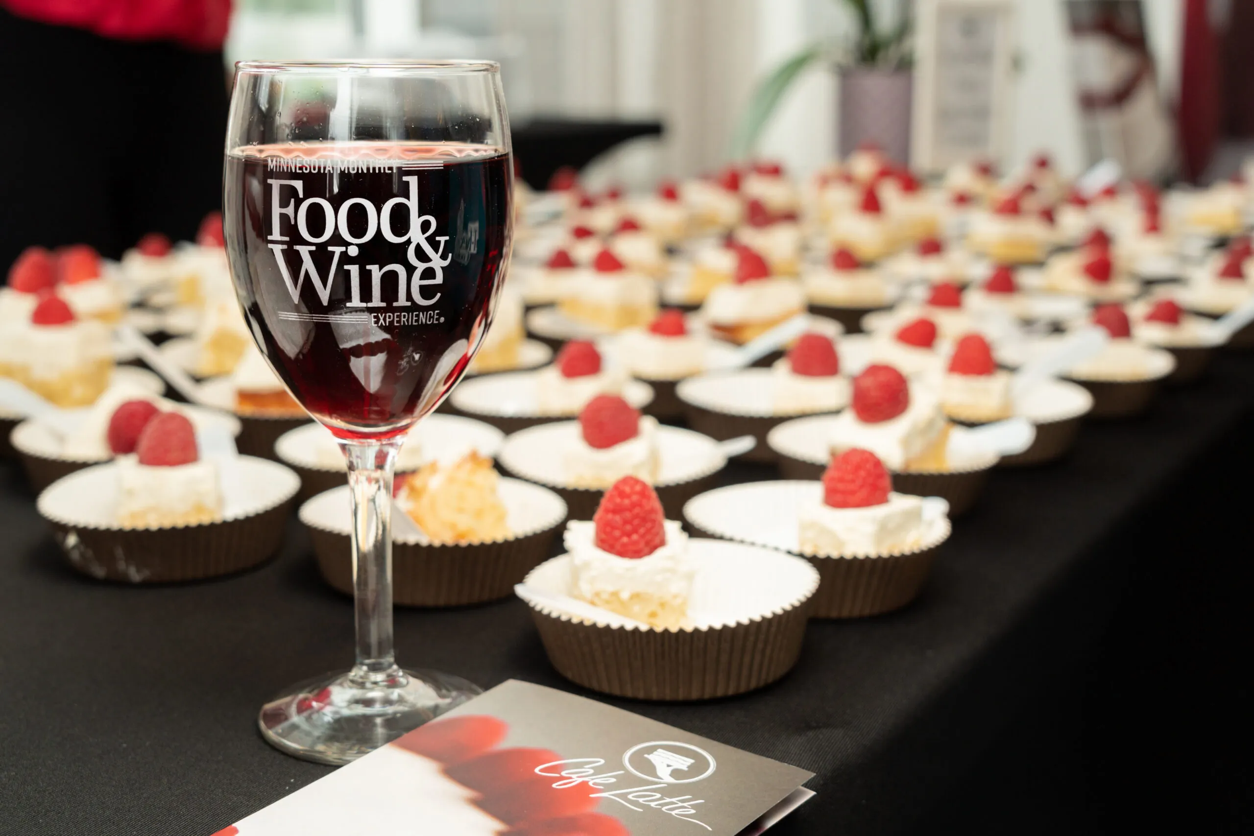 A wine glass with "Food & Wine Experience" printed on it at table full of desserts