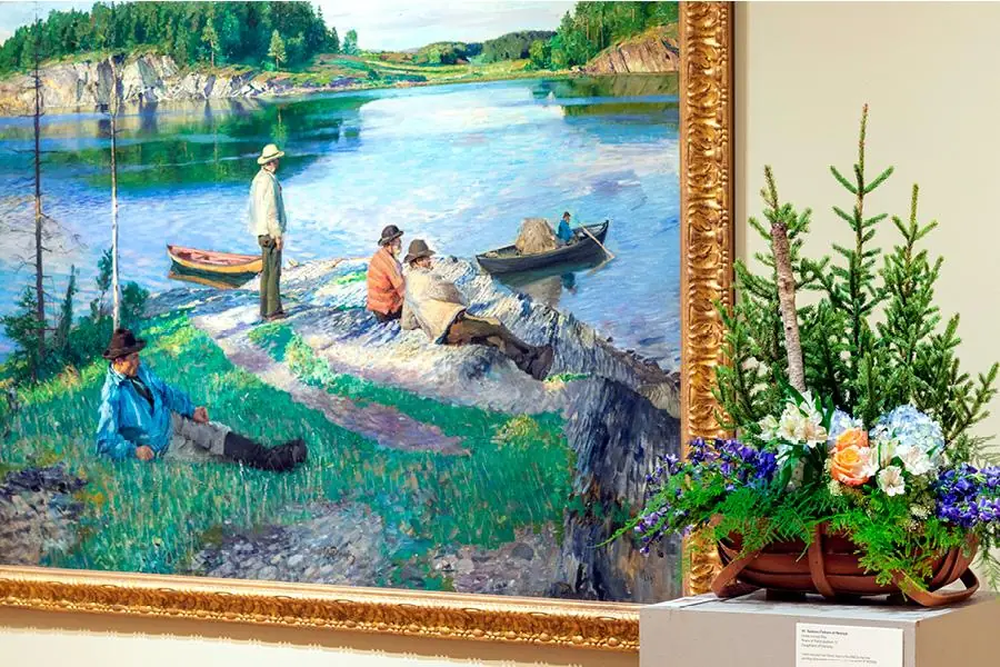 A landscape oil painting hangs next to a corresponding floral arrangement