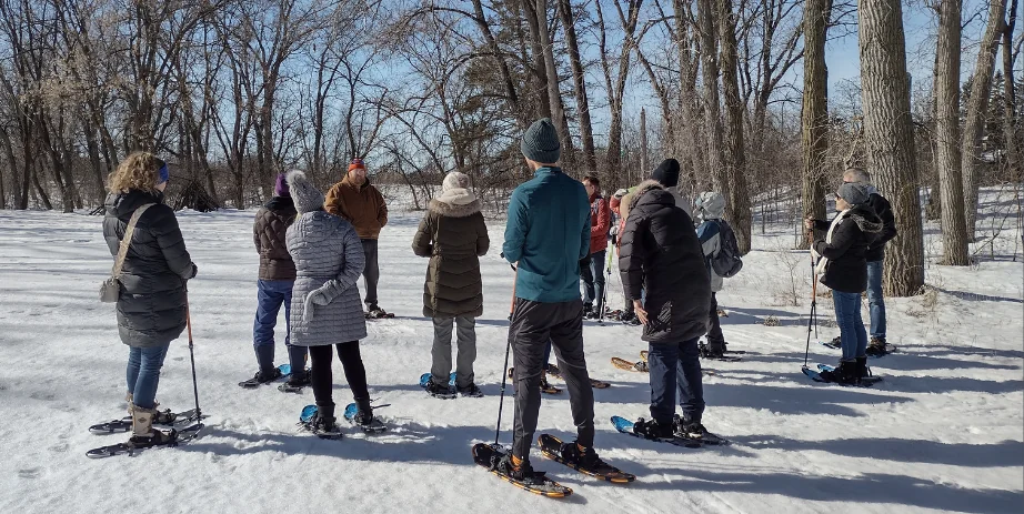 A group of people on snowshoes stand in the snow