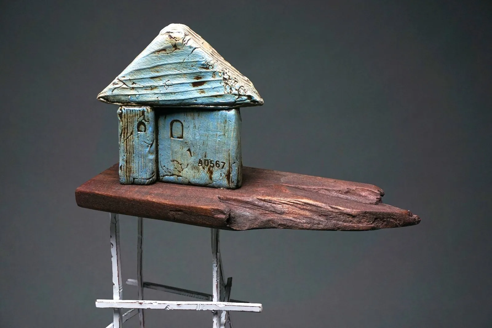 A sculpture of a blue house on top of a piece of wood