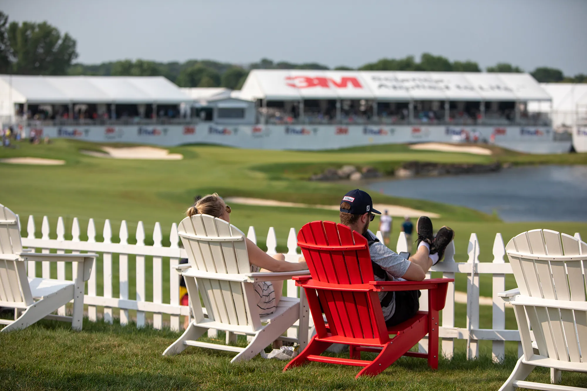 Two people lounging in Adirondack chairs near a golf course