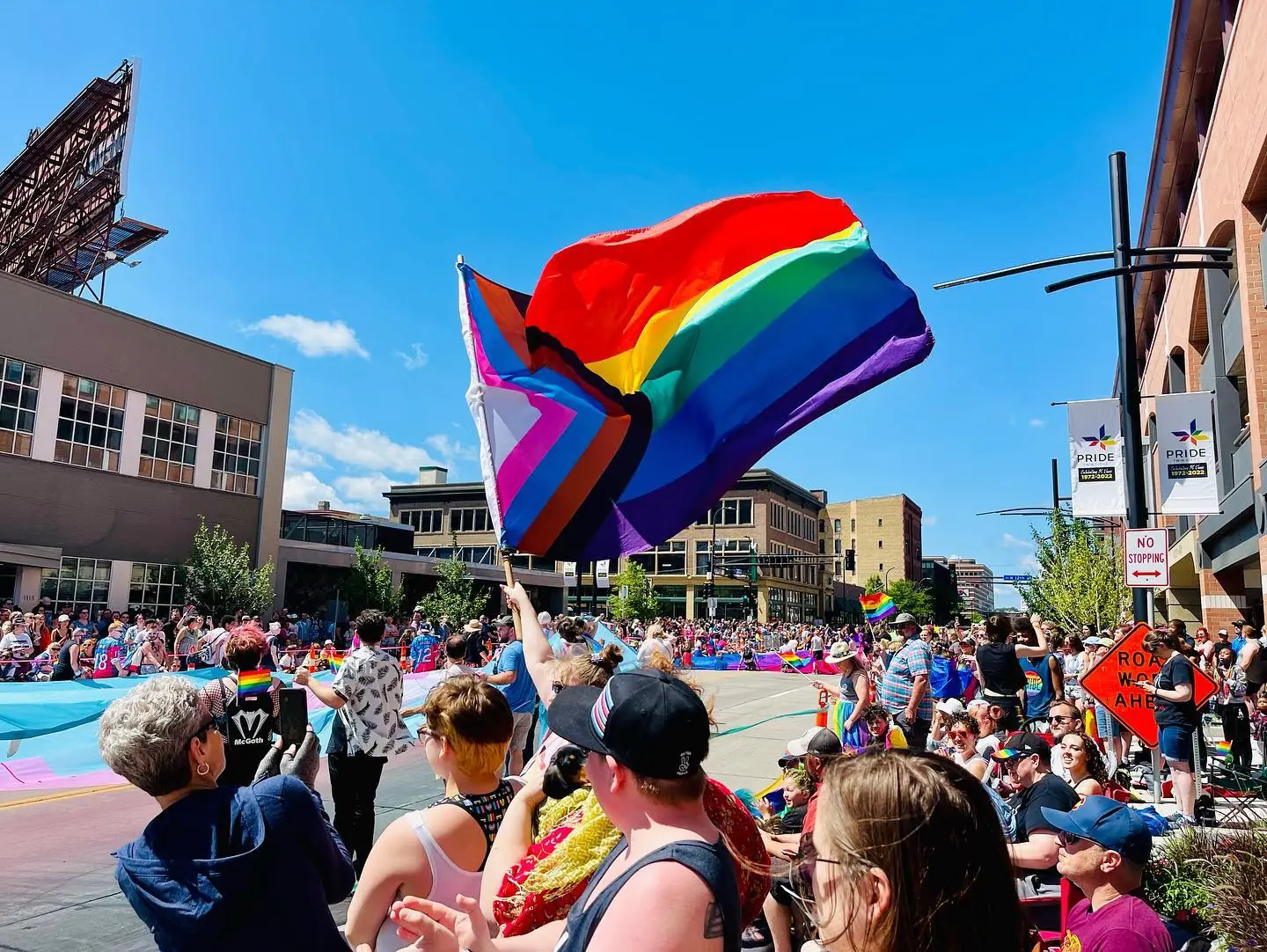 A group of people cheering at a parade. One waves a pride flag.