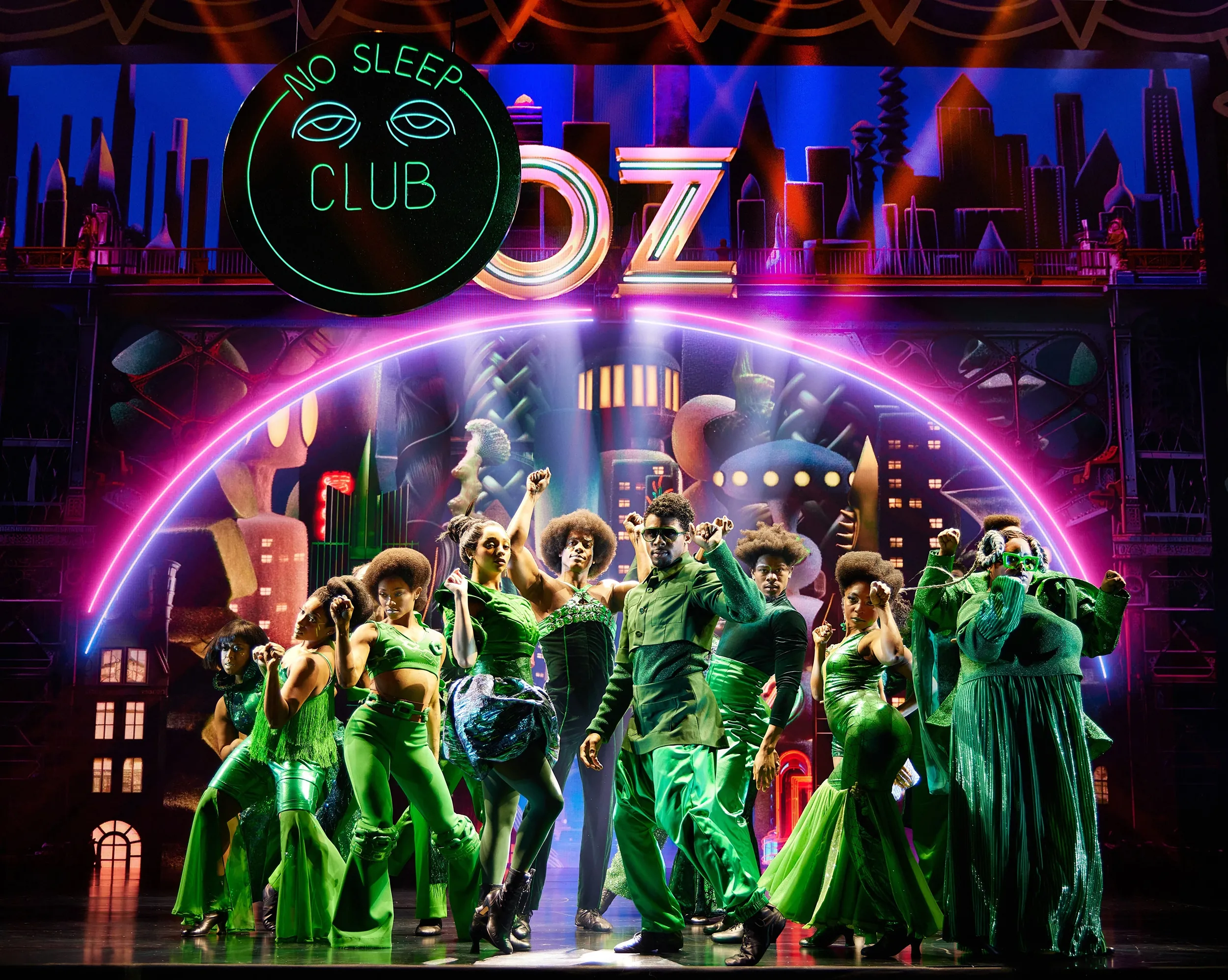 A group of people dressed in green outfits pose in front of a sign that says Oz/No Sleep Club