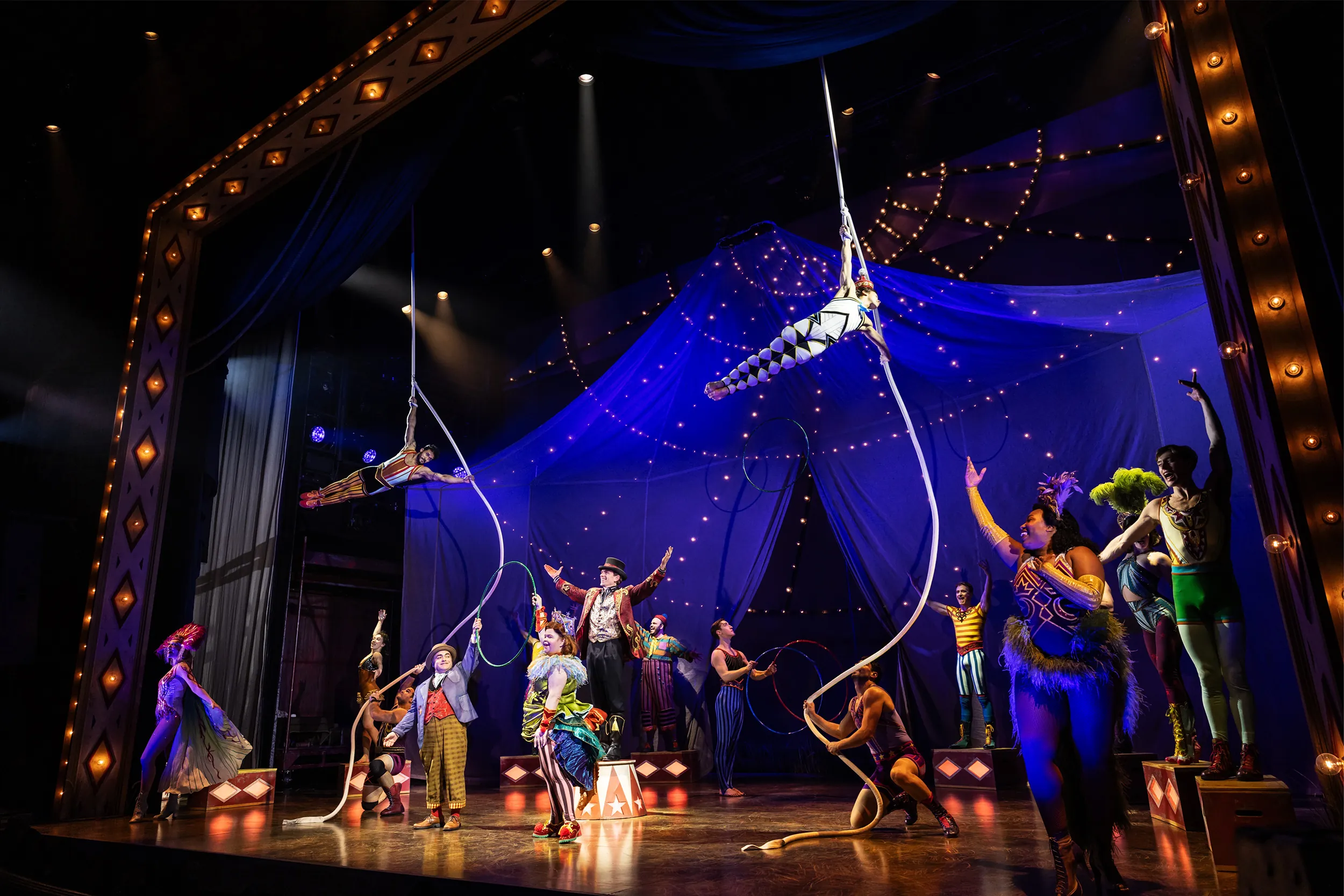 Acrobats dangle from robes hanging from the ceiling as circus performers dance