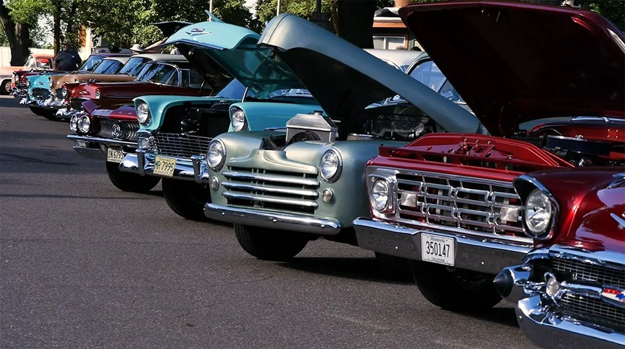 A line of 50s-era cars with hoods popped